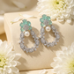 Pair of earrings with turquoise stones and pearls on a beige surface with white flowers.